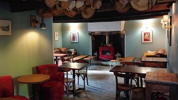 Een gezellig restaurant met houten tafels en stoelen, een open haard en hoeden die aan het plafond hangen.