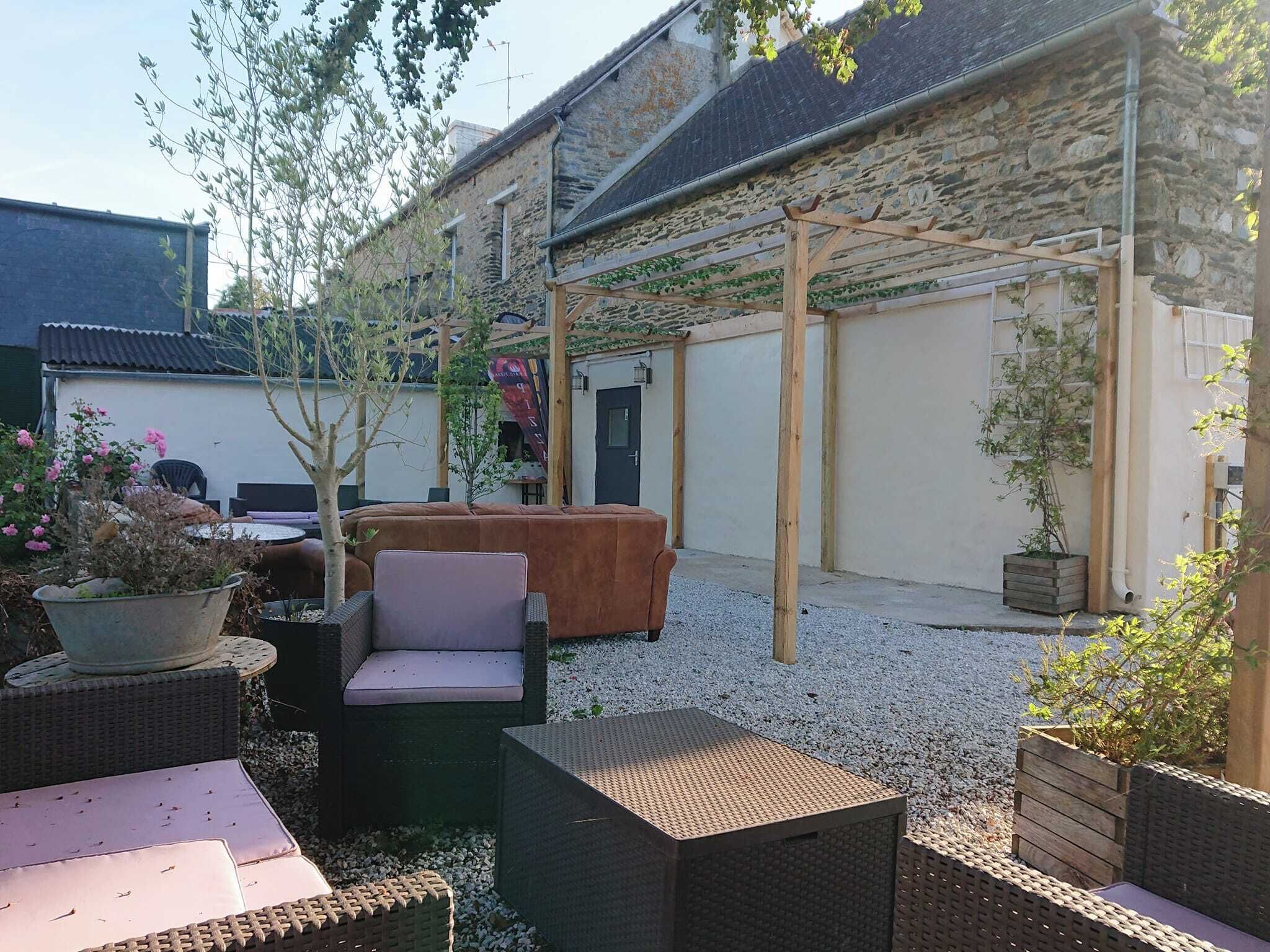 A courtyard with wicker furniture, a wooden pergola, and a stone building.