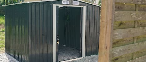 A metal shed with a door, gravel base, and a wooden fence in the background.