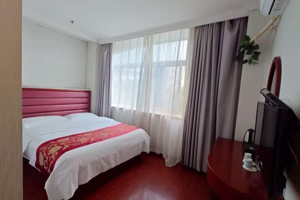 A hotel room with a bed, a desk, a chair, a television, and a window with curtains.