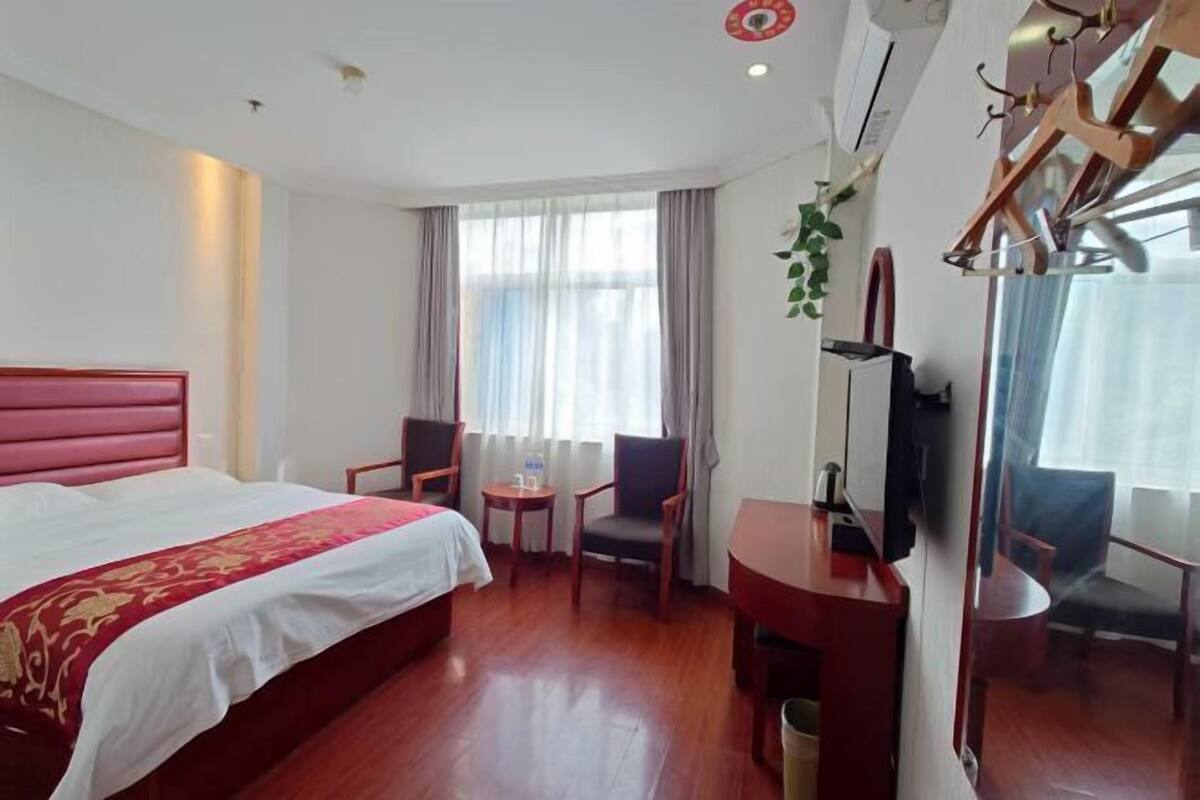 A hotel room with a large bed, a desk, a chair, a small table, and a TV.