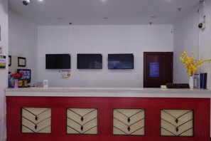 A reception desk with three monitors, a red counter, and a vase with yellow flowers. - Shangji Hotel (Waigaoqiao Bonded Area North Metro Station Branch) (Shanghai)