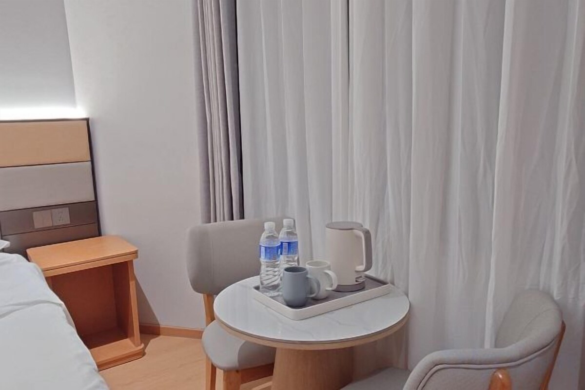 A hotel room with a bed, a small table with a tray containing a mug and water bottles, and a chair.