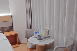 Habitación de hotel con cama, una mesita con una bandeja que contiene una taza y botellas de agua, y una silla.