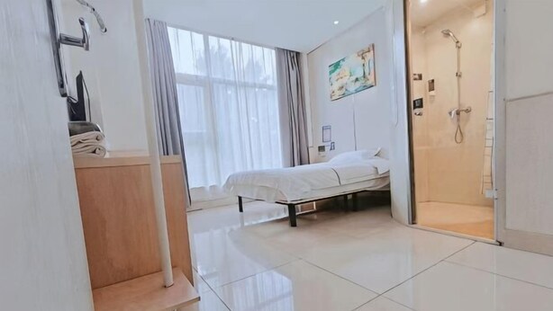 Een hotelkamer met een bed, een douche, een houten kast en een groot raam met gordijnen.