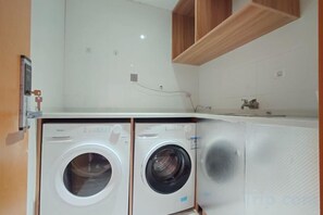 A compact laundry area with two washing machines, a small sink, and wooden cabinets. - Shangji Hotel (Waigaoqiao Bonded Area North Metro Station Branch) (Shanghai)