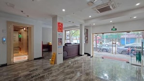 Een hotel lobby met een marmeren vloer, een receptiebalie, een zithoek en uitzicht op de straat.