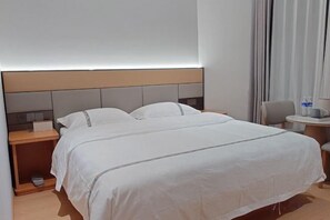 A hotel room with a bed, a nightstand, a chair, and a small table with a lamp. - Shangji Hotel (Waigaoqiao Bonded Area North Metro Station Branch) (Shanghai)