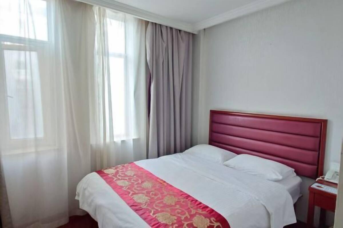 A hotel room with a bed, curtains, a nightstand, and a window.