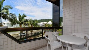 A balcony with a white tiled floor, a round table, and two white plastic chairs.