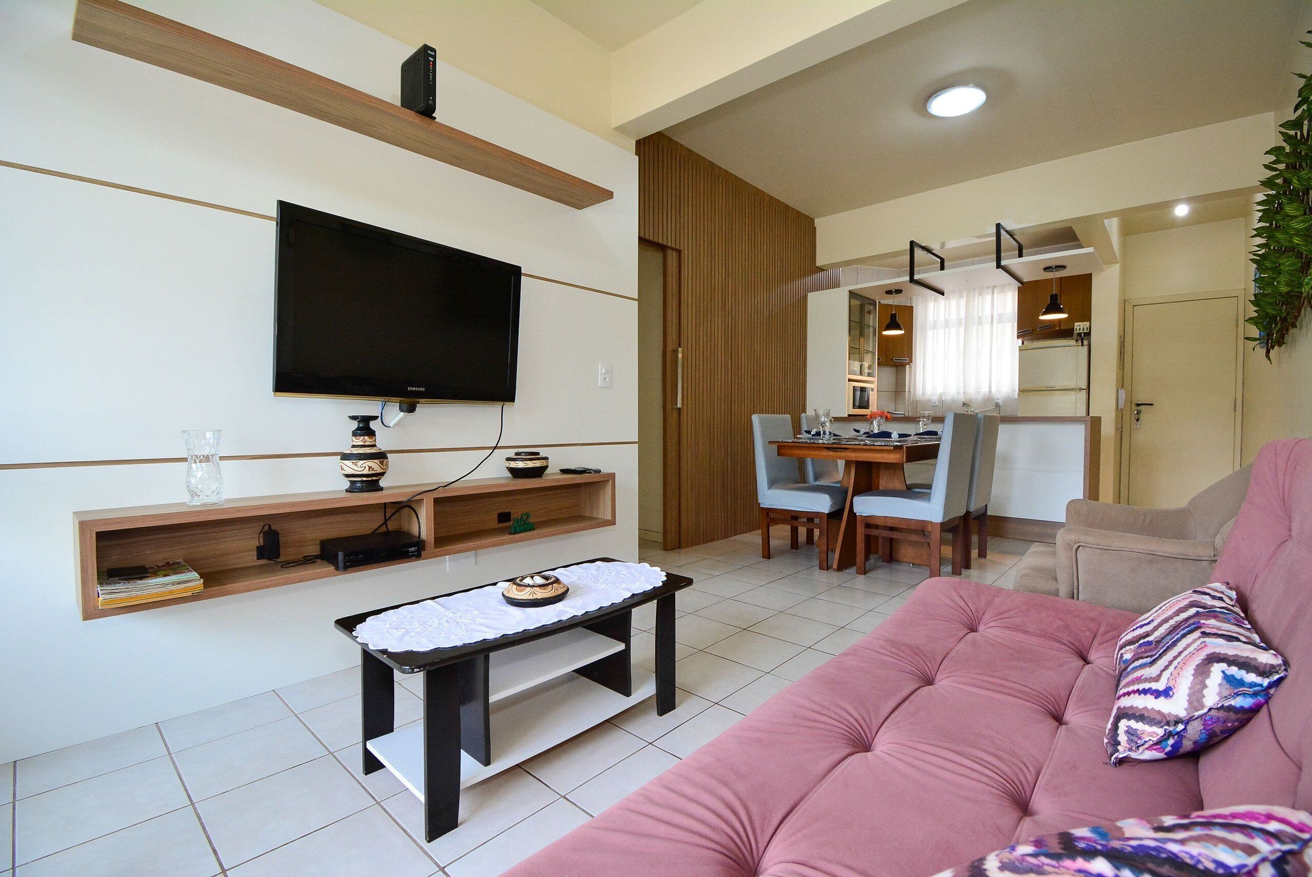 A modern living room with a flat-screen TV, a wooden shelf, a small table, and a pink sofa.