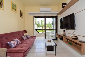 A living room with a red sofa, a coffee table, a TV, and a balcony with a view of palm trees. - Refúgio Terra do Sol (Florianópolis)
