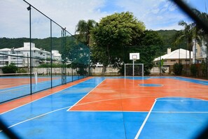Una cancha de baloncesto al aire libre con superficie azul y naranja, rodeada por una cerca de malla metálica.