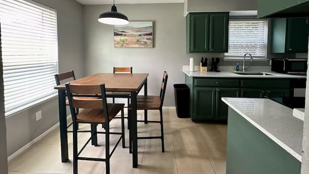 Une cuisine compacte avec des meubles de couleur verte, une table à manger en bois et un luminaire suspendu.