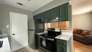 Une cuisine de taille réduite avec des meubles de couleur vert foncé, un réfrigérateur en acier inoxydable et une cuisinière noire.
