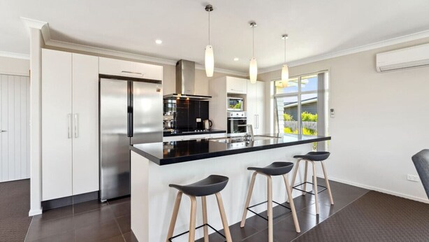 A modern kitchen with a central island, stainless steel appliances, and bar stools. - Delight in the Dell - 2 mins to lake (Taupō)