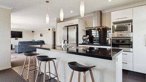 A modern kitchen with a central island, bar stools, stainless steel appliances, and pendant lighting. - Delight in the Dell - 2 mins to lake (Taupō)