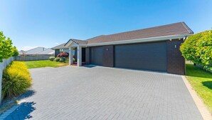 A residential house with a paved driveway, a garage, and a well-maintained lawn. - Delight in the Dell - 2 mins to lake (Taupō)
