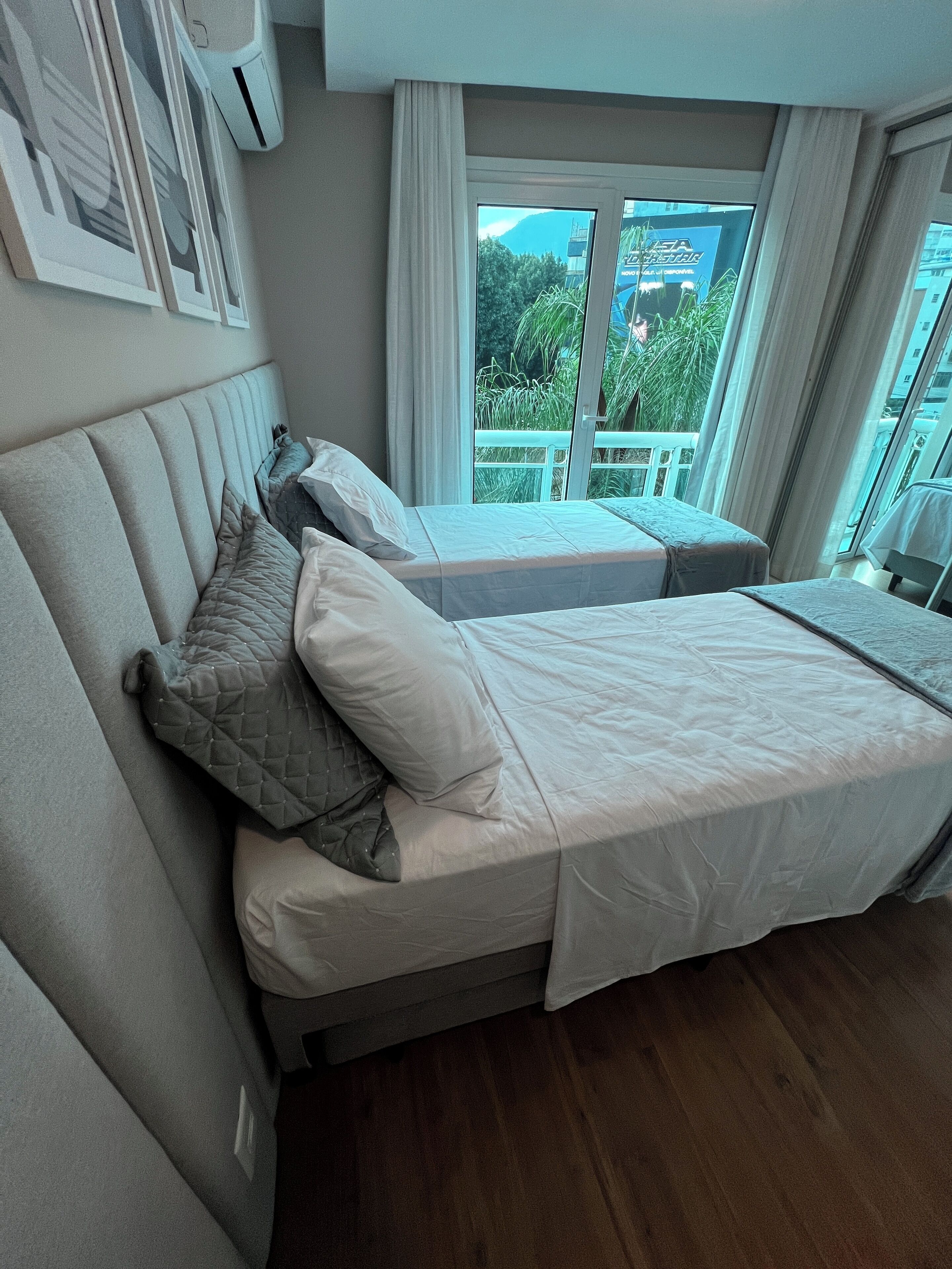 Ein Hotelzimmer mit einem großen Bett, einem kleineren Bett und einem Fenster mit Blick auf Grünflächen.