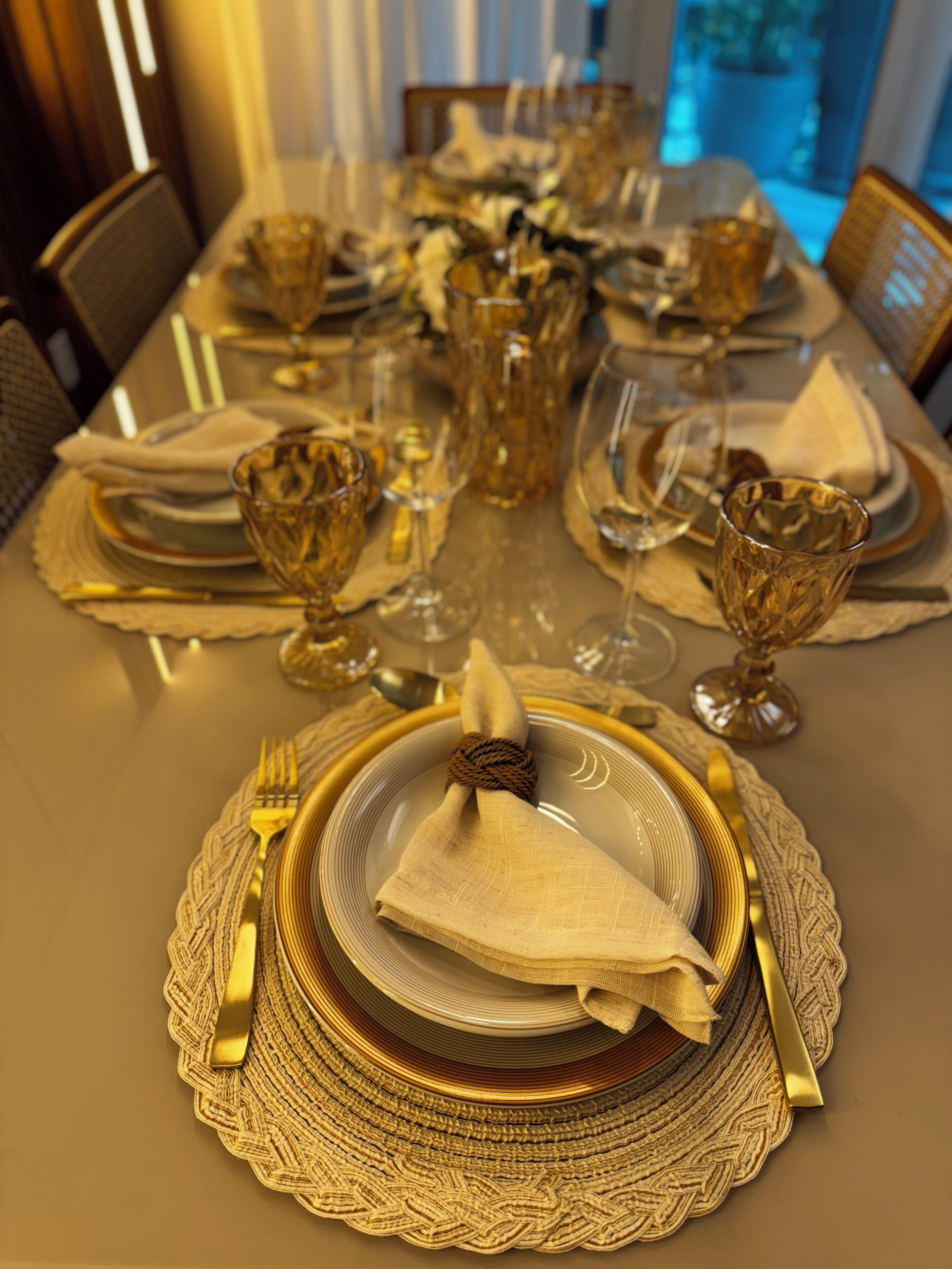 A formal dining table set with gold and white tableware, including plates, glasses, and cutlery.