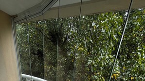Een balkon met glazen hekwerk met uitzicht op een weelderige tuin.