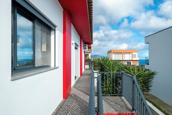 Ein modernes Gebäude mit roter und weißer Fassade, einem schmalen Weg und einem Blick auf das Meer im Hintergrund.