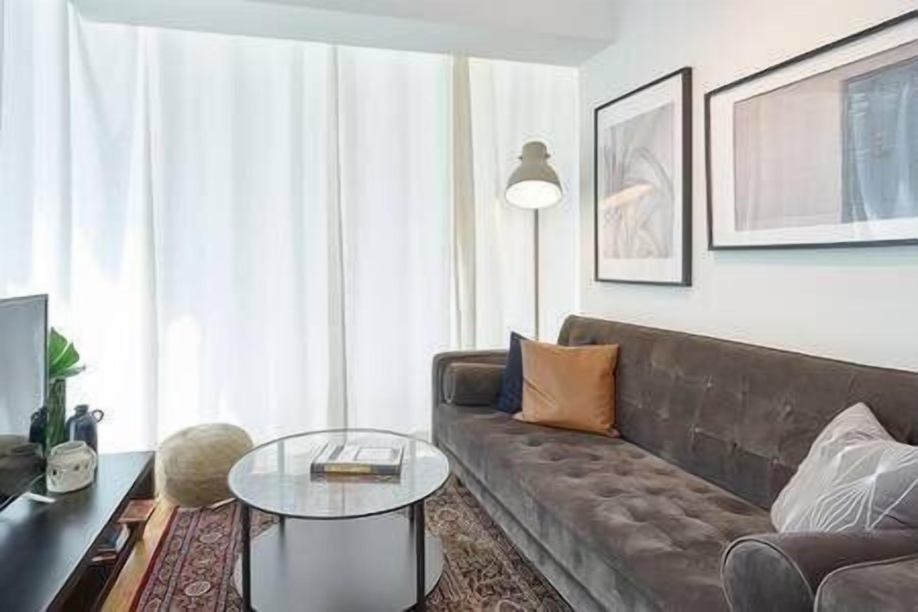 Ein Wohnzimmer mit einer Couch, einem Glastisch, einer Lampe und gerahmten Kunstwerken an der Wand.