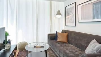Ein Wohnzimmer mit einer Couch, einem Glastisch, einer Lampe und gerahmten Kunstwerken an der Wand.