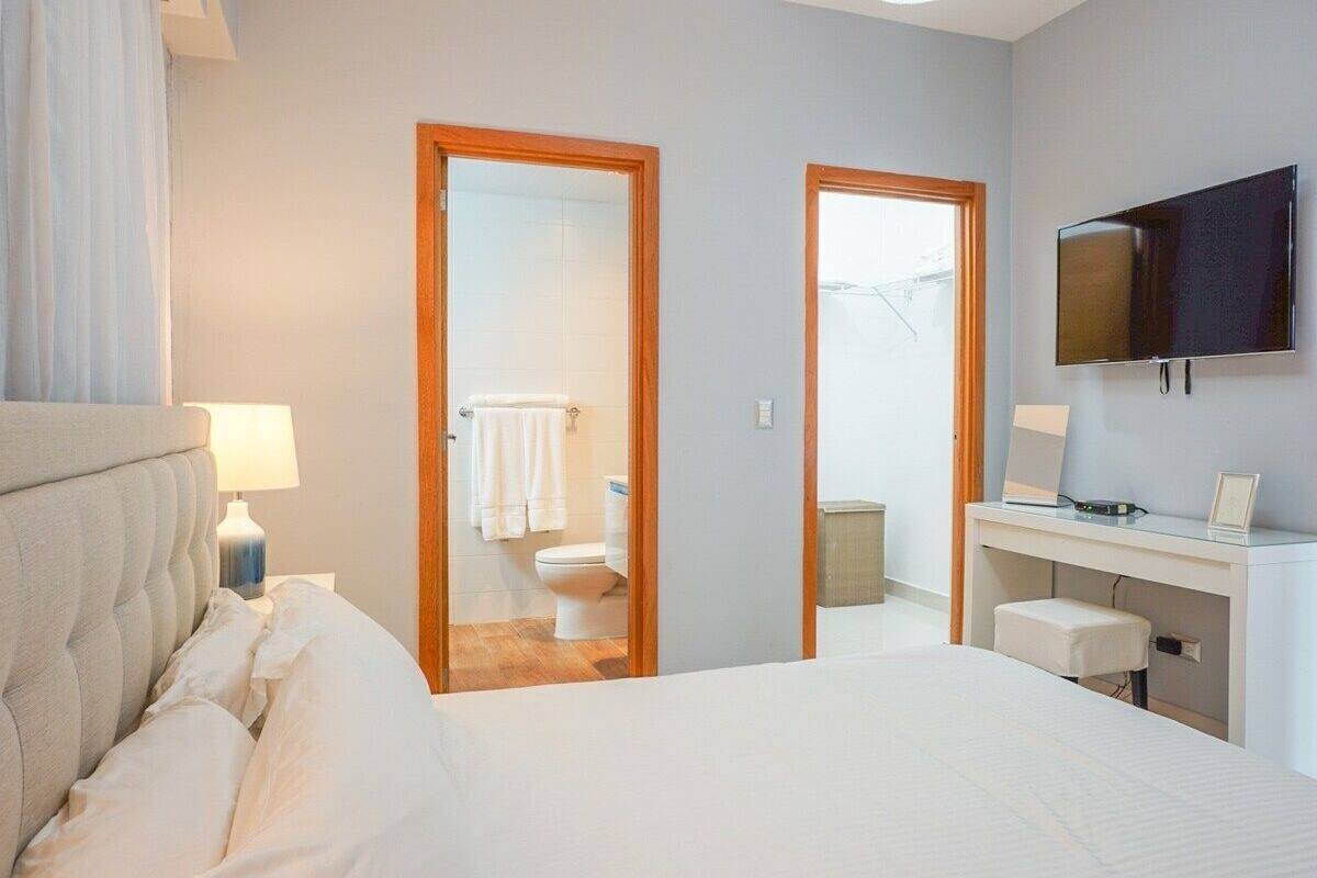 A hotel room with a bed, a desk, a TV, and a bathroom visible through an open door.