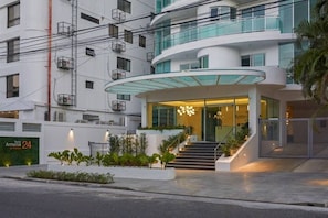 A modern hotel with a curved glass entrance, multiple balconies, and a staircase leading to the entrance. - Torre Armonia 24 (Santo Domingo)