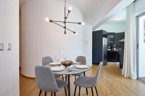 A modern dining area with a round glass table set for four, grey upholstered chairs, and a contemporary chandelier. - Torre Armonia 24 (Santo Domingo)