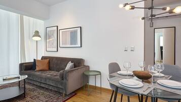 Een moderne woonkamer met een grijze bank, een glazen salontafel en een eethoek met borden en glazen.