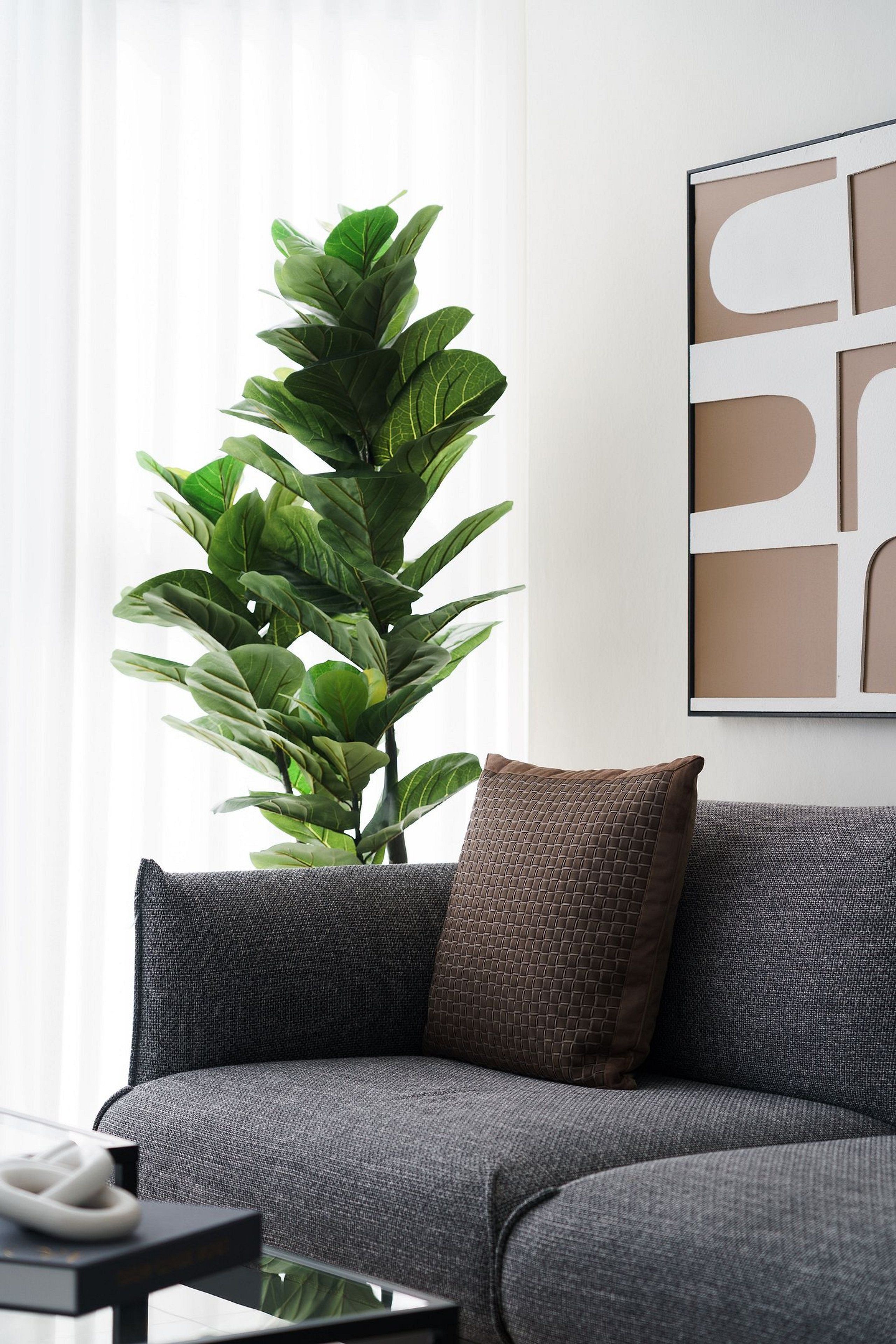 A modern living room with a grey sofa, a large green plant, and a framed abstract artwork on the wall.
