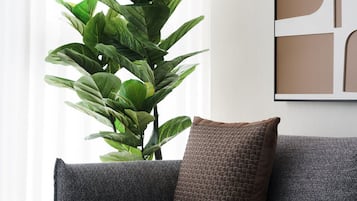 A modern living room with a grey sofa, a large green plant, and a framed abstract artwork on the wall.