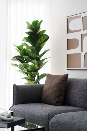 A modern living room with a grey sofa, a large green plant, and a framed abstract artwork on the wall. - Torre Armonia 24 (Santo Domingo)