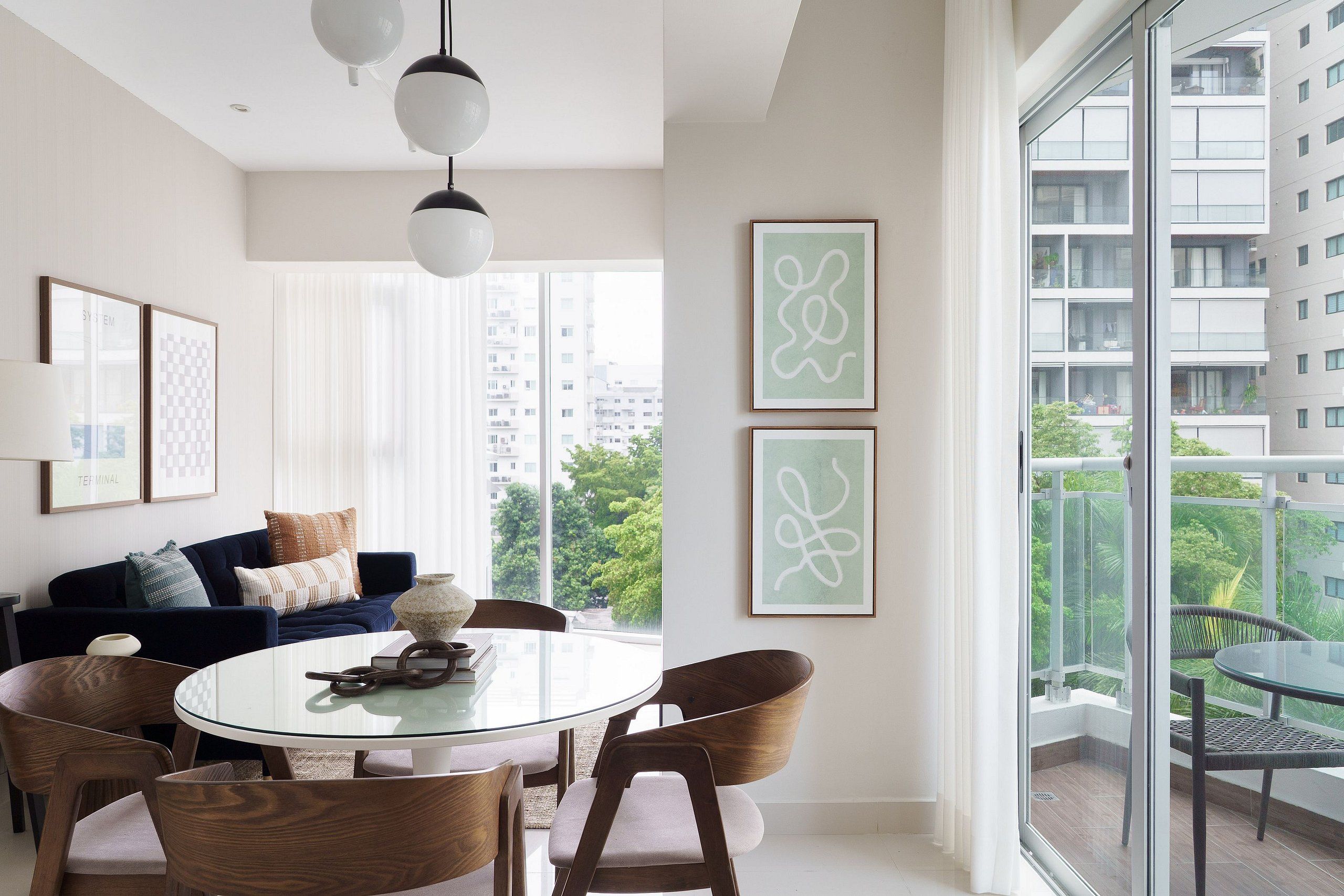 A modern living room with a round glass table, wooden chairs, a dark blue sofa, and a city view through large windows.
