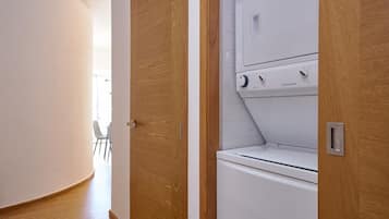 A laundry room with a white washing machine and dryer, wooden doors, and a small table with chairs in the background.