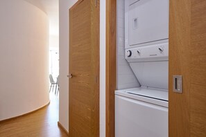A laundry room with a white washing machine and dryer, wooden doors, and a small table with chairs in the background. - Torre Armonia 24 (Santo Domingo)