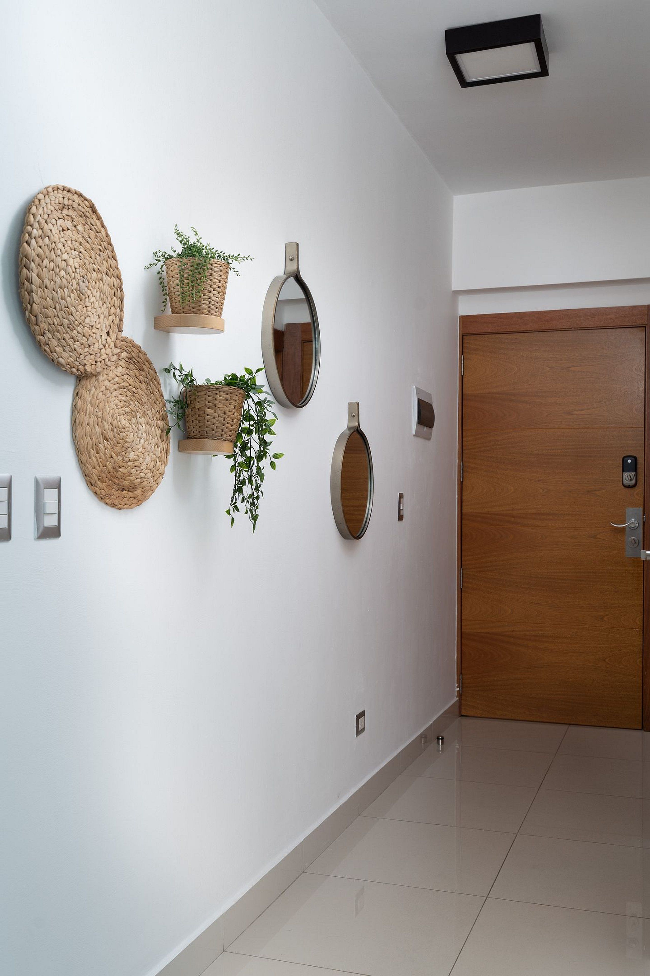 A hallway with a wooden door, a wall-mounted mirror, and woven wall art.
