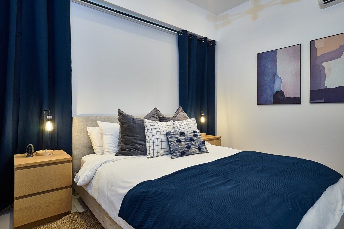A modern bedroom with a bed, nightstands, and artwork on the wall.