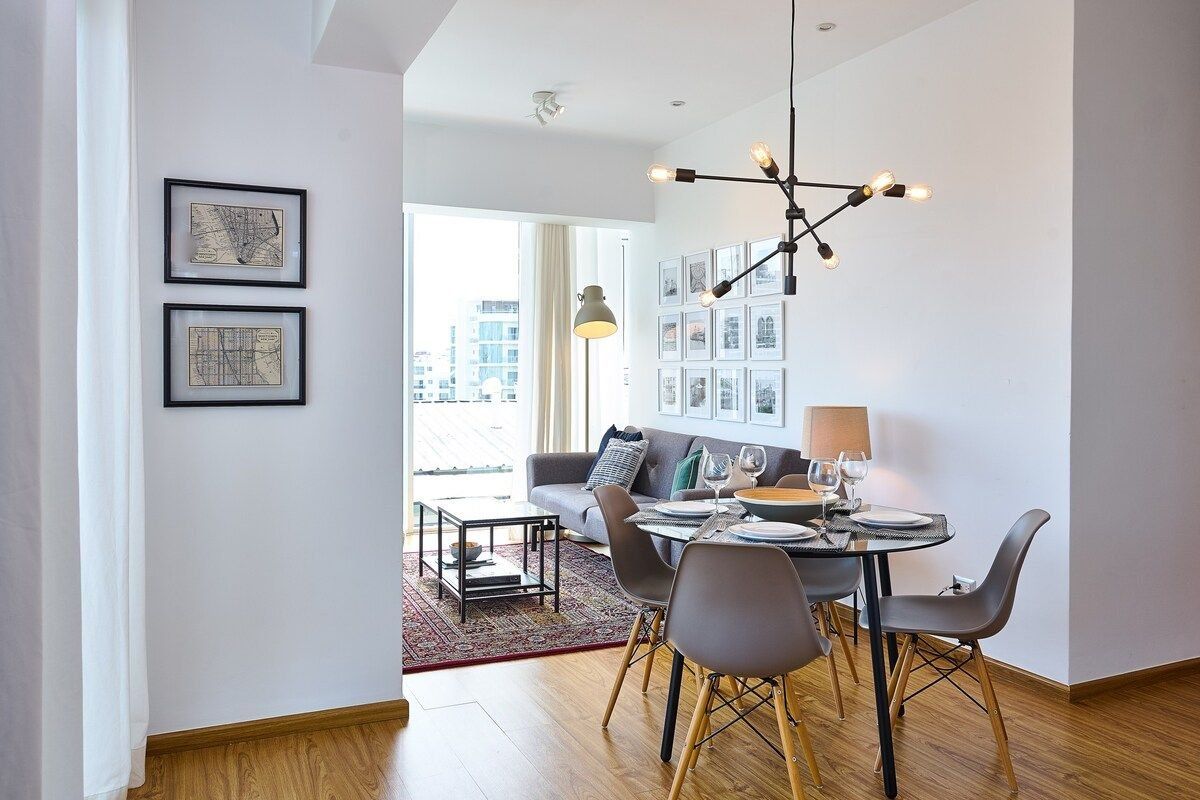 Un espace de restauration moderne avec une table ronde, des chaises grises et une vue sur la ville grâce à de grandes fenêtres.