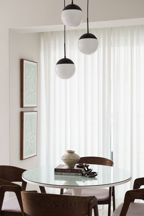 A dining area with a glass table, wooden chairs, and pendant lights. - Torre Armonia 24 (Santo Domingo)