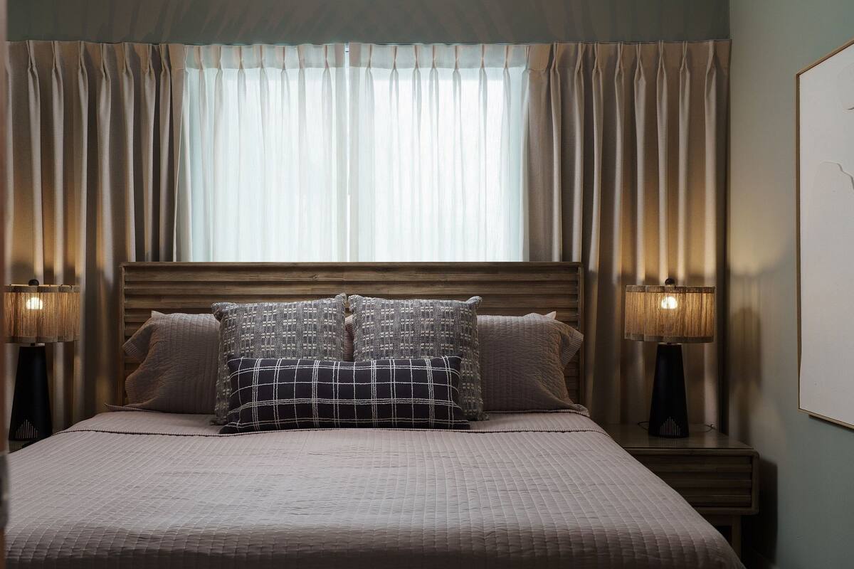 A neatly made bed with a quilted bedspread and two decorative pillows, flanked by two bedside lamps on wooden nightstands.
