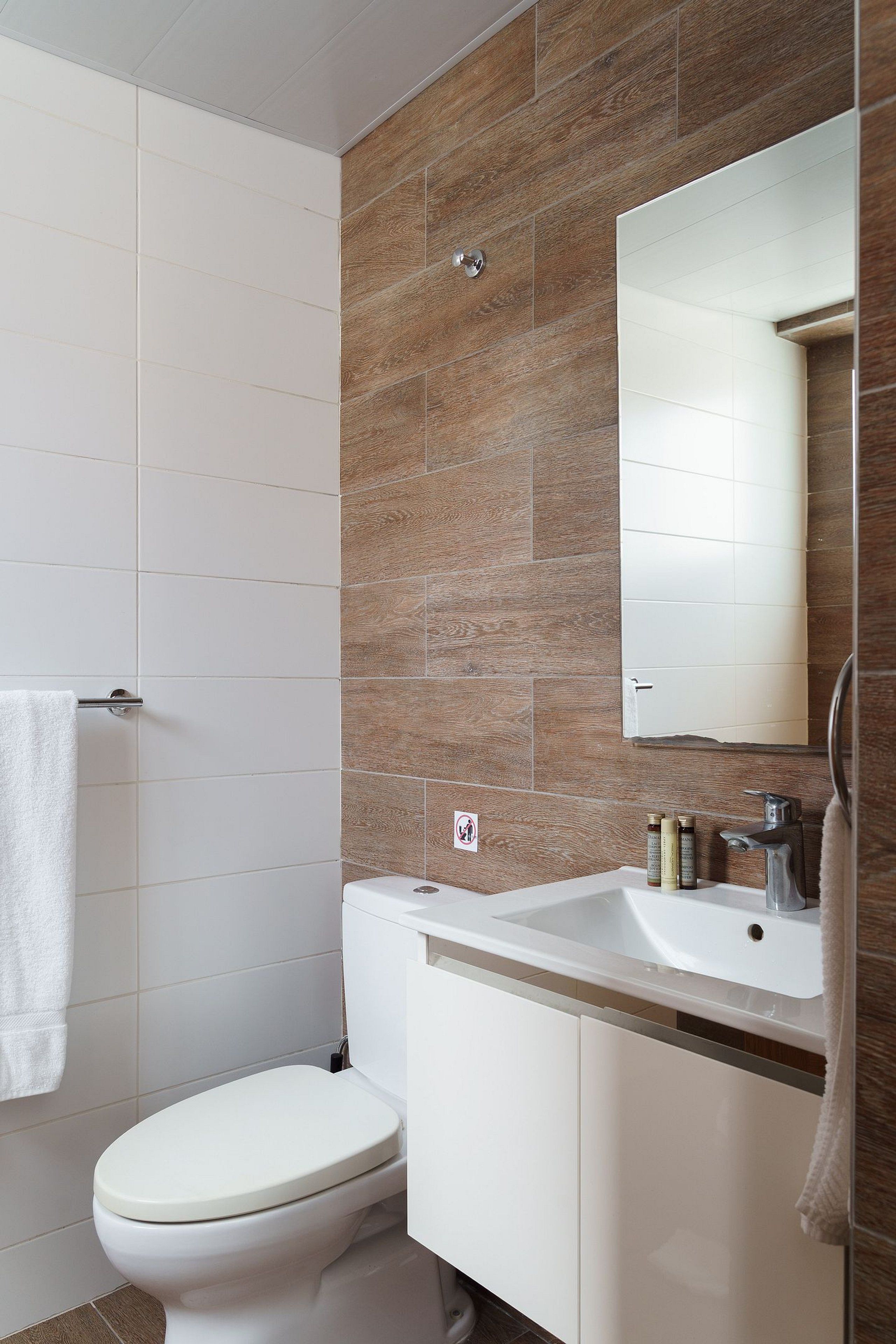 Un baño moderno con inodoro blanco, lavabo con espejo y zona de ducha.