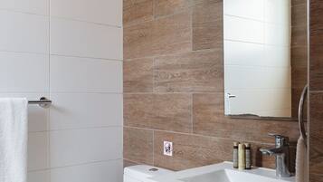 Un baño moderno con inodoro blanco, lavabo con espejo y zona de ducha.