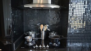 A kitchen with a black tiled backsplash, stainless steel appliances, and a range hood. - Torre Armonia 24 (Santo Domingo)