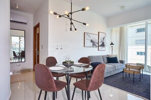 A modern living room with a dining area, featuring a chandelier, a sofa, and a view of the city. - Torre Armonia 24 (Santo Domingo)