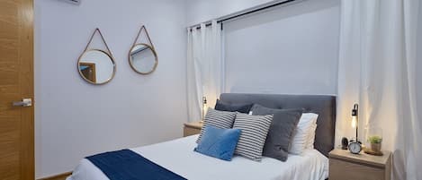 Ein modernes Schlafzimmer mit Bett, Nachttischen, einem Beistelltisch mit Lampe und einer Wand-Klimaanlage.