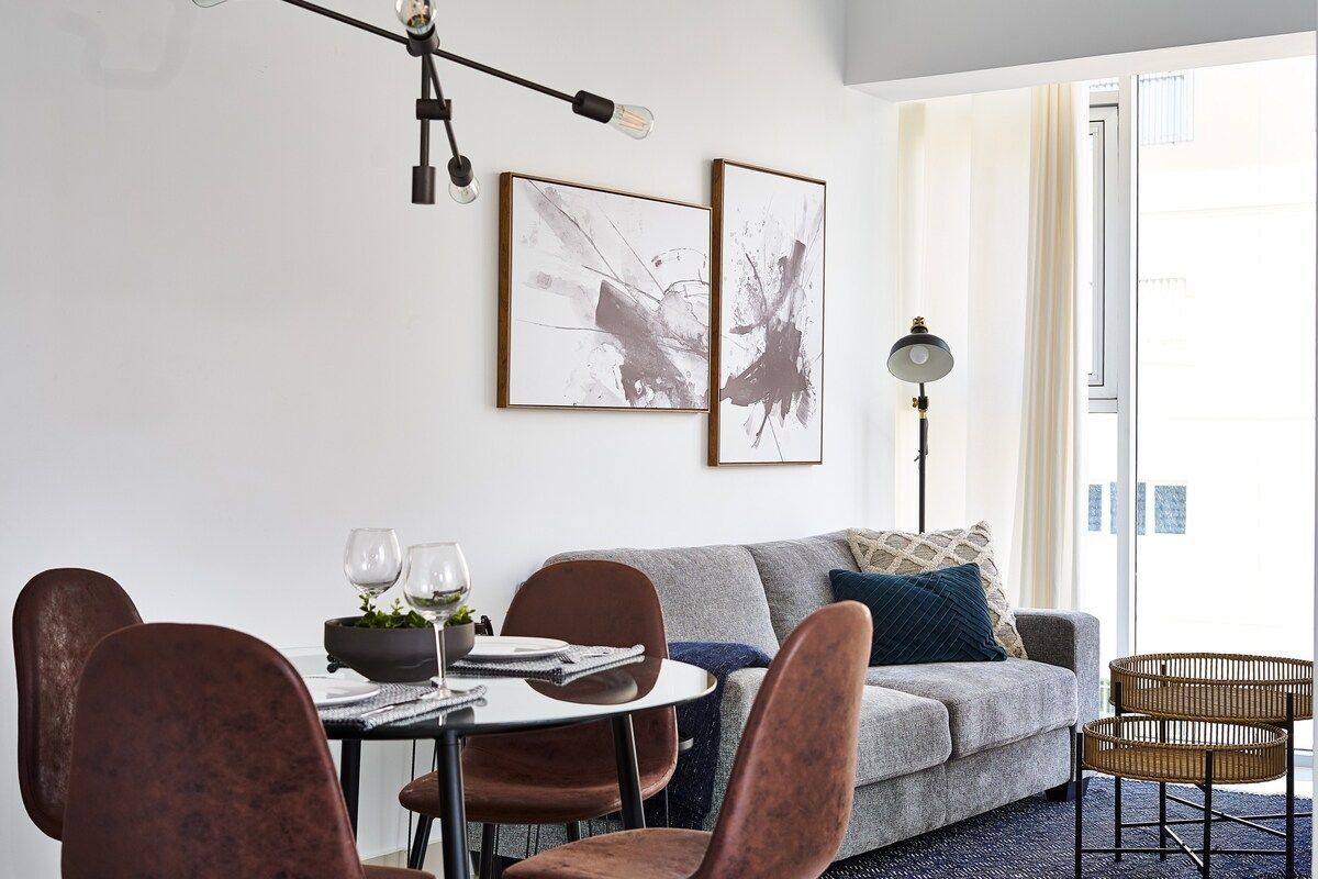 Ein modernes Wohnzimmer mit einem grauen Sofa, einem Esstisch mit Stühlen und zwei abstrakten Bildern an der Wand.