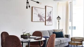 Ein modernes Wohnzimmer mit einem grauen Sofa, einem Esstisch mit Stühlen und zwei abstrakten Bildern an der Wand.